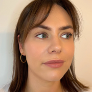 A close-up image of a person wearing large 22 karat gold hoop earrings.